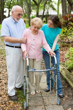 Elderly couple walking with carer. Lady is using zimmer frame.